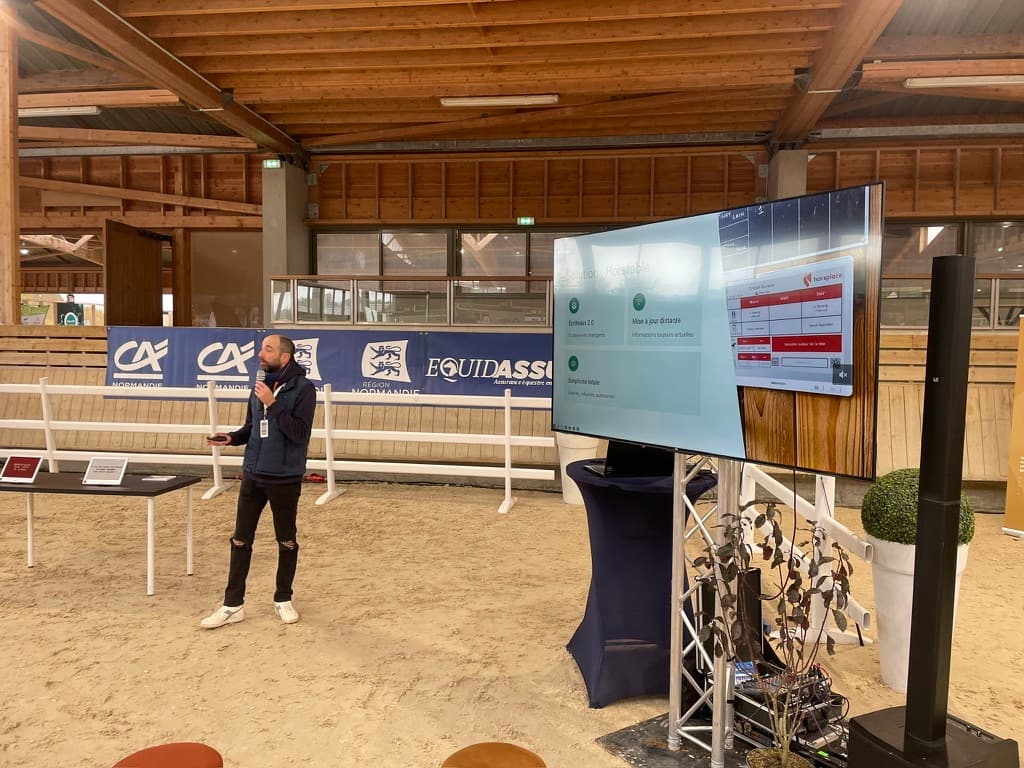 Vincent Bray au micro dans la carrière du Pôle International du Cheval, devant un grand écran montrant l’application Horstable